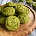 Spinach banana muffins served on a wooden plate. Some muffins cooling on a wire rack in the background.