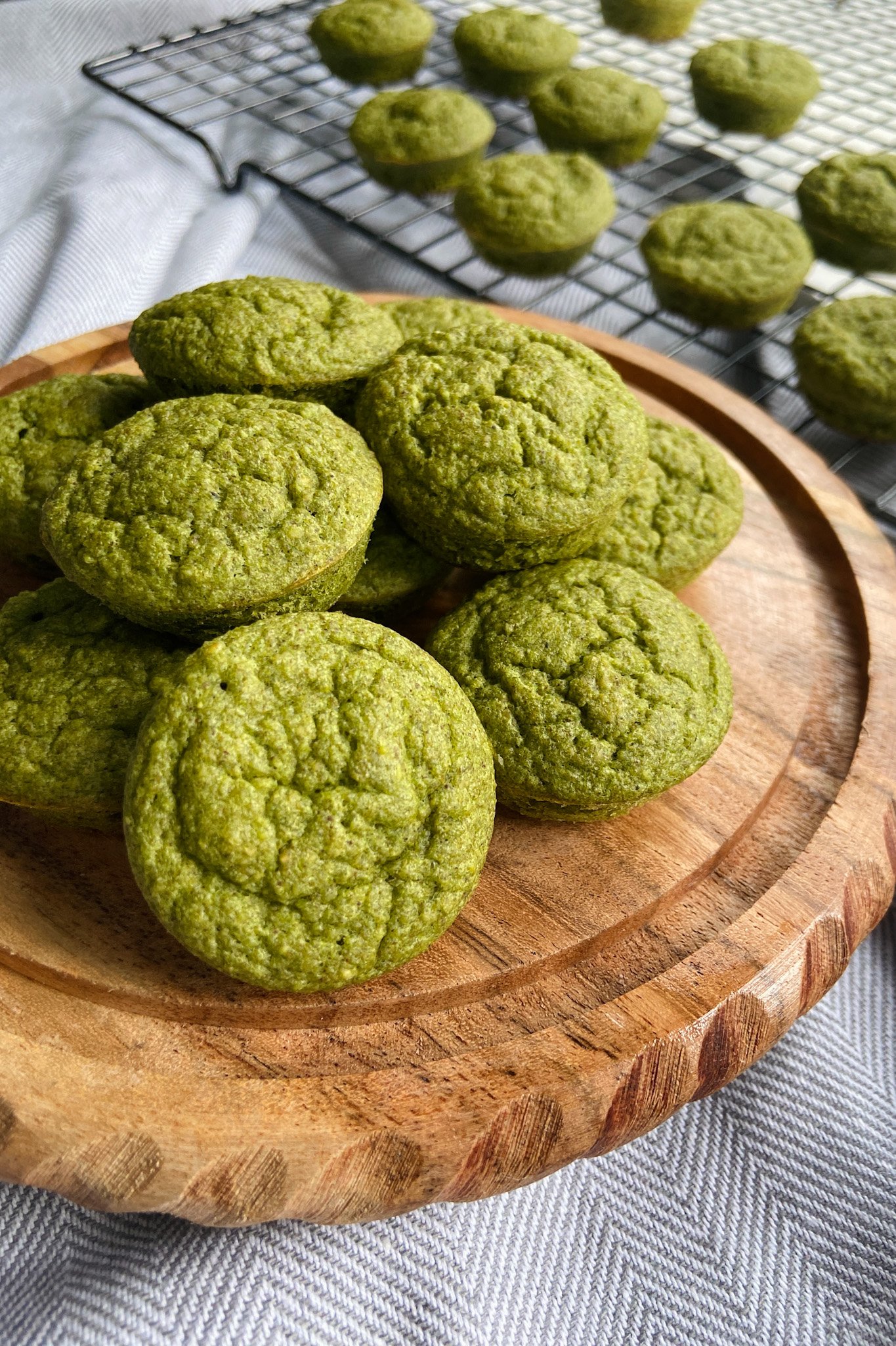 Spinach banana muffins served on a wooden plate. Some muffins cooling on a wire rack in the background.