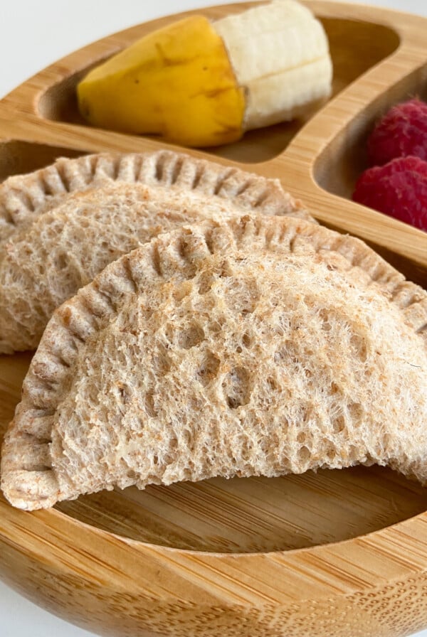 Peanut butter and empanada sandwiches served with a side of banana and raspberries