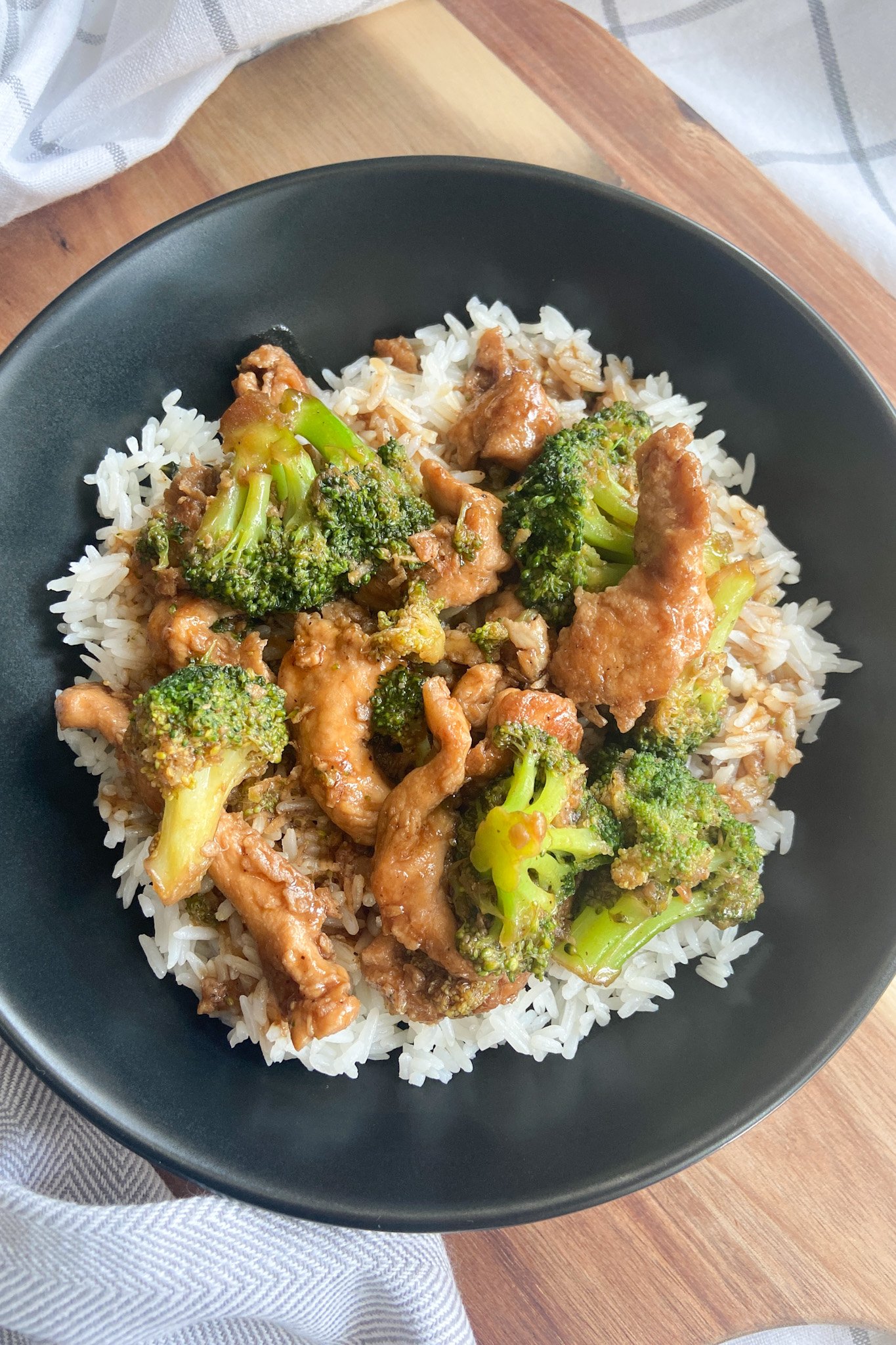 Chicken and broccoli stir-fry served oven white rice in a black bowl.