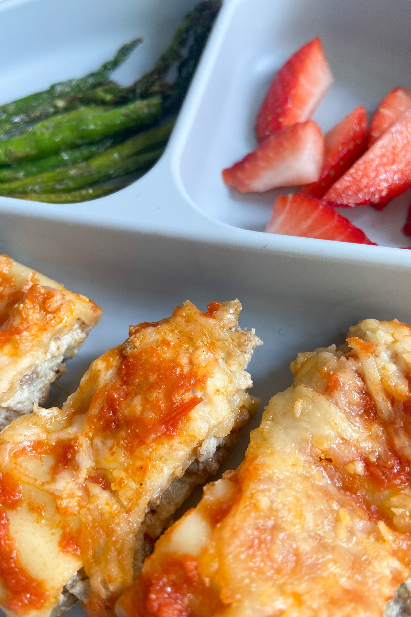 Cheesy beef manicotti served with asparagus and sliced strawberries