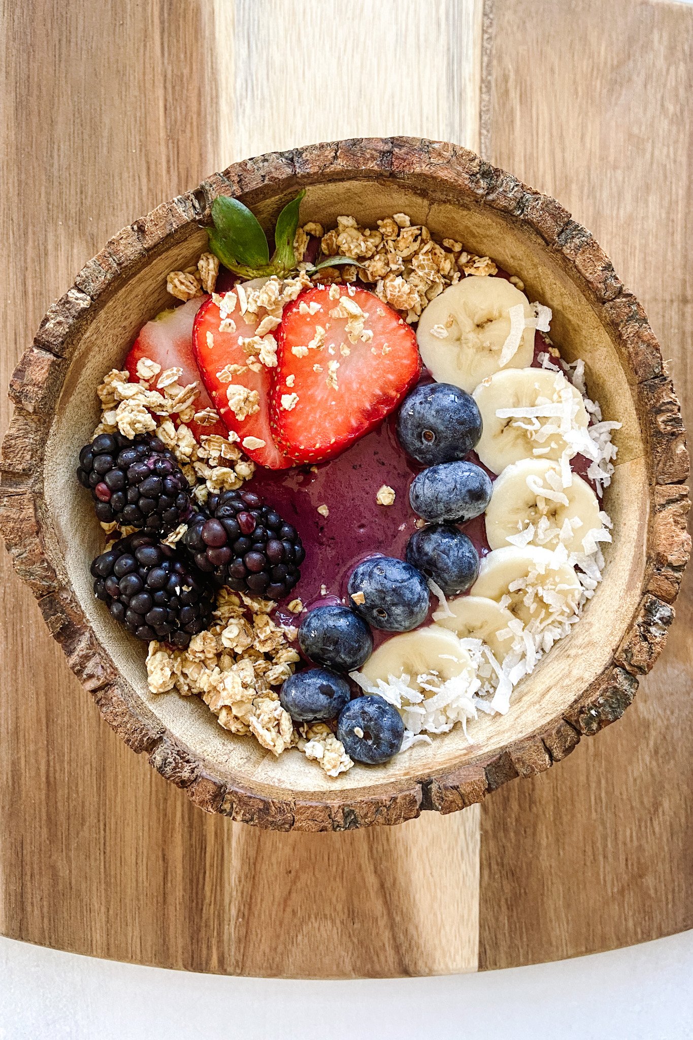 Acai bowl topped with granola, sliced bananas, blueberries, blackberries and strawberries