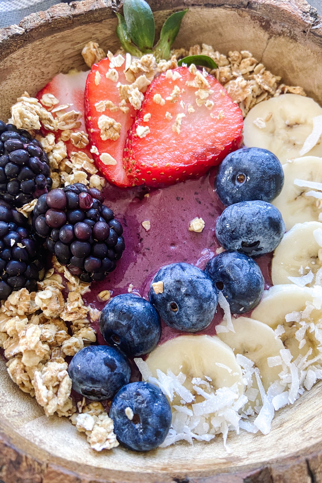 Acai bowl topped with granola, sliced bananas, blueberries, blackberries and strawberries