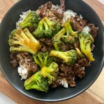 Beef and broccoli stir-fry served over white rice in a black plate.