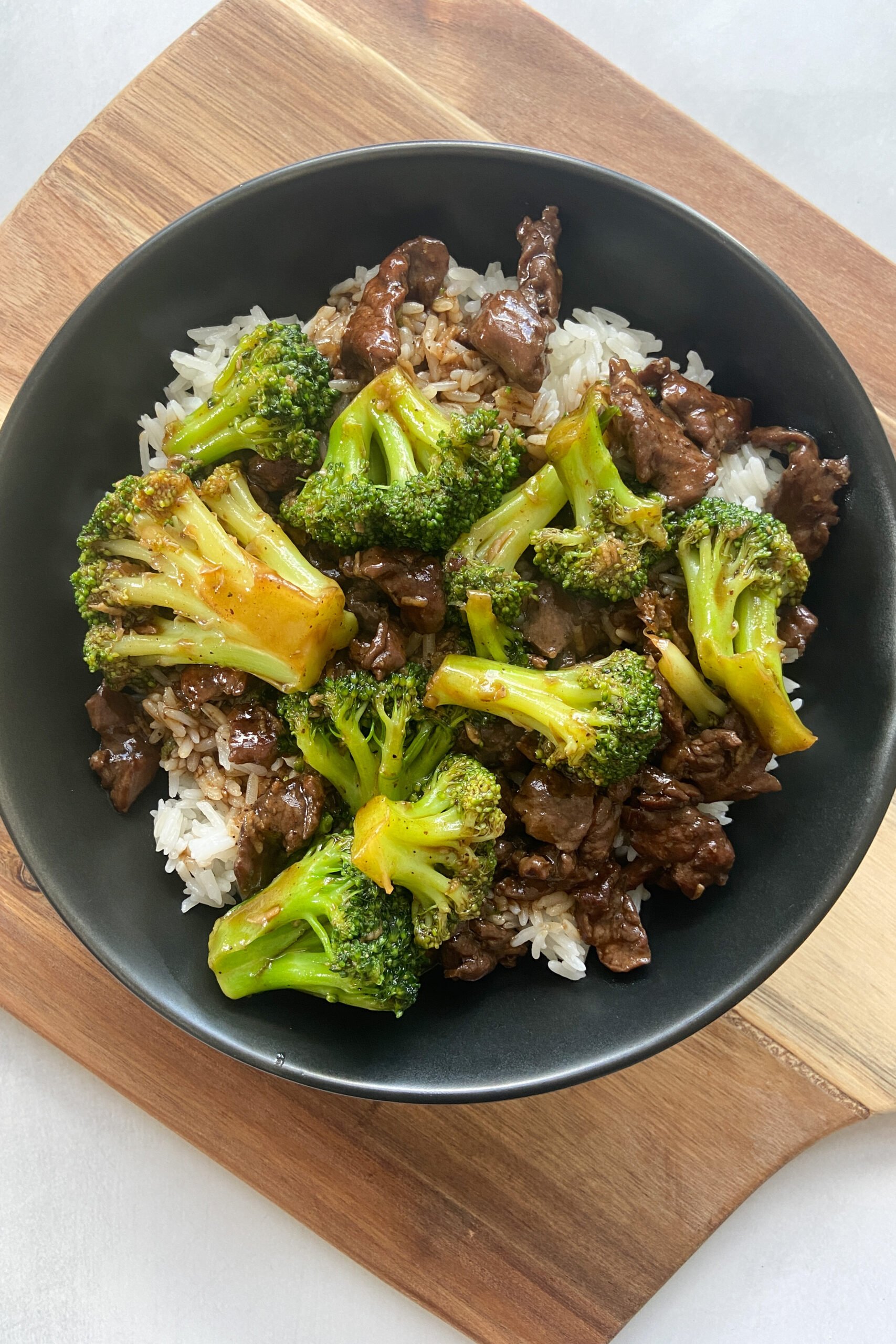 Beef and broccoli stir-fry served over white rice in a black plate.