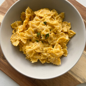 Creamy pumpkin pasta garnished with parsley flakes. Served in a gray bowl.