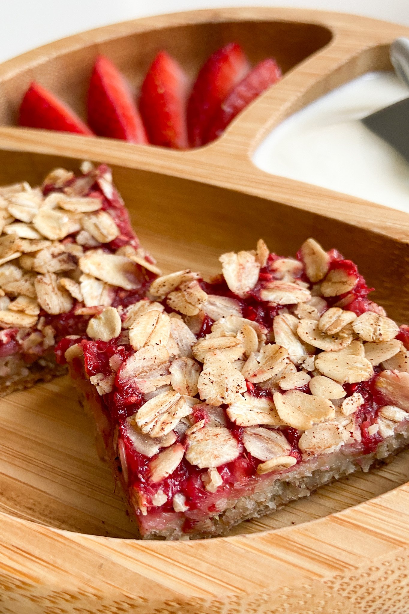Raspberry oat bars plated with sliced strawberries and yogurt.