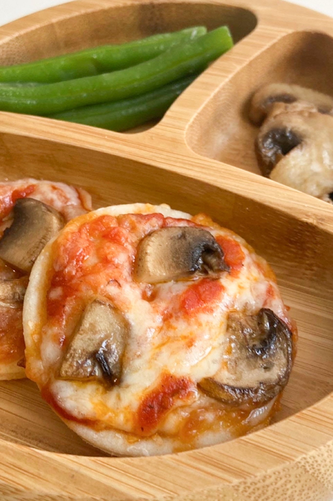 Mini pizzas topped with mushrooms and served with green means and sautรฉed mushrooms.