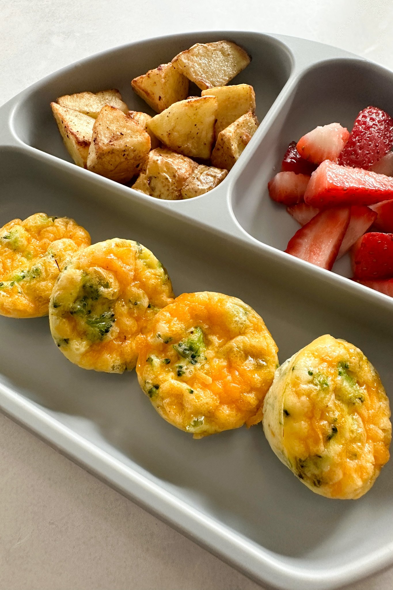 Broccoli egg bites served with fruits and potatoes.