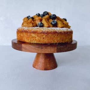 Apple almond cake on a cake stand topped with cinnamon apples and fresh berries.