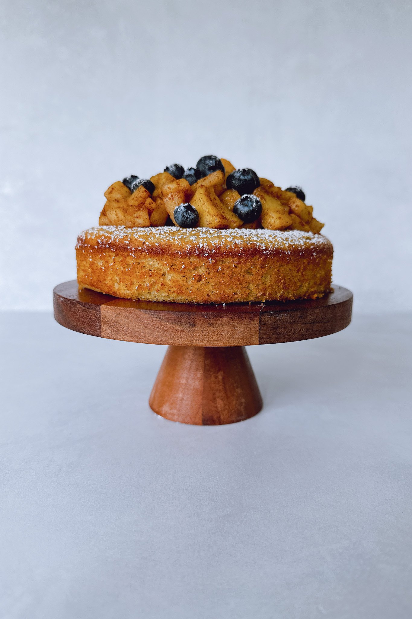 Apple almond cake on a cake stand topped with cinnamon apples and fresh berries.