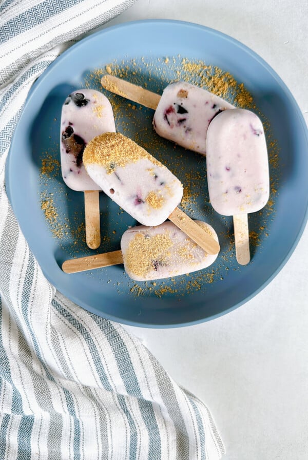 Mini blueberry cheesecake popsicles on a blue plate.
