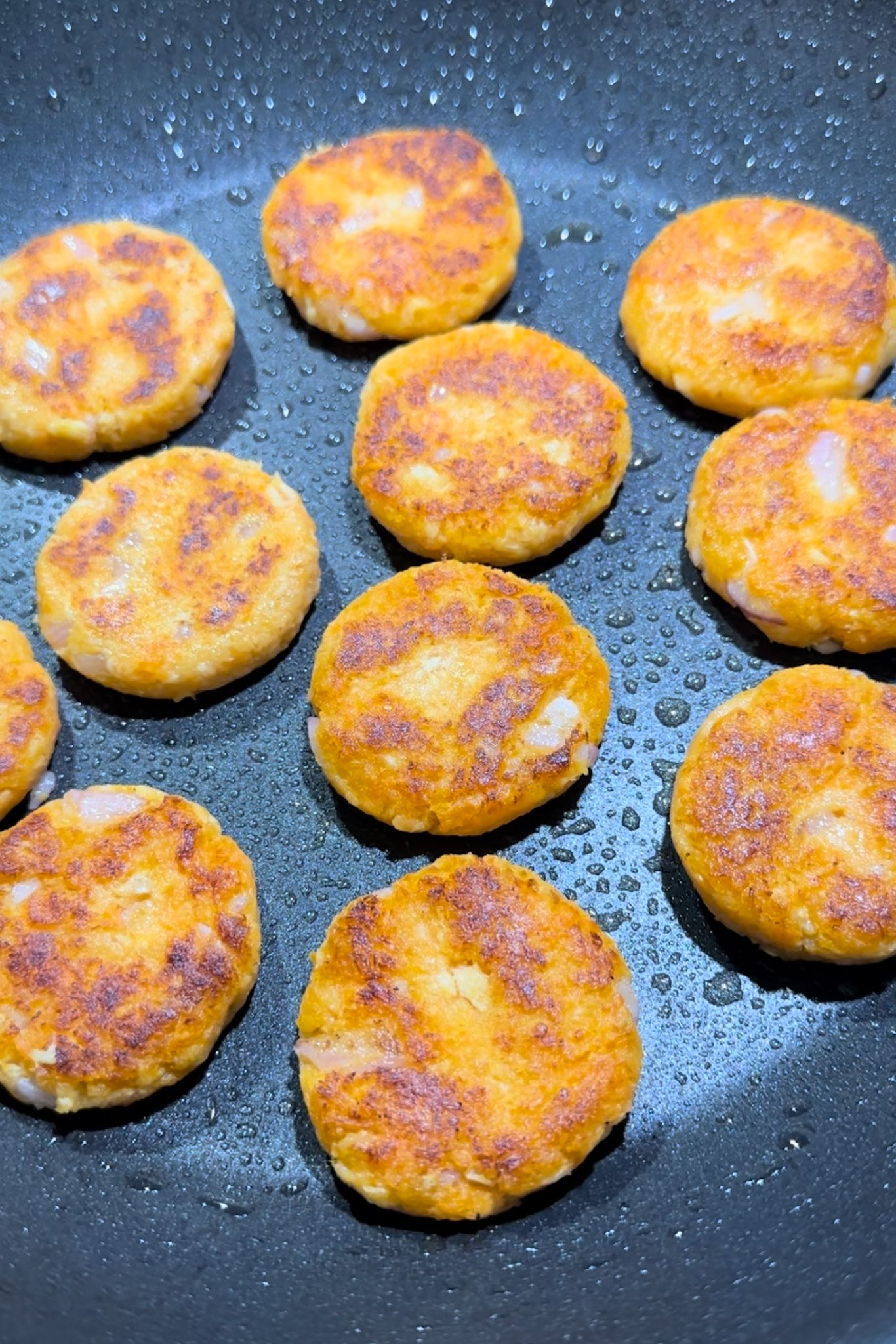 Sweet potato salmon cakes cooking in pan.