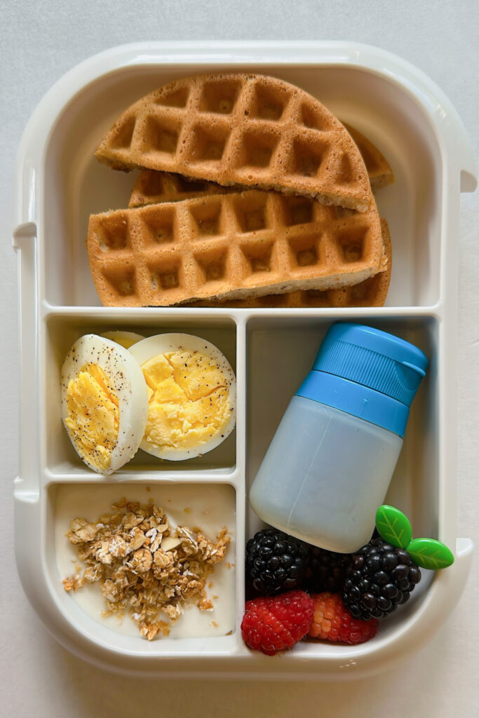 Eggless waffles, eggs, yogurt with granola, raspberries, raspberries, and maple syrup.