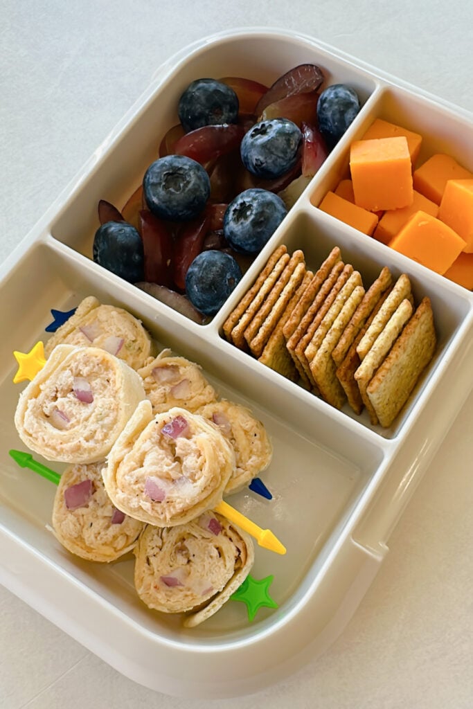 Chicken salad rollups served with crackers, cheese, blueberries, and grapes.