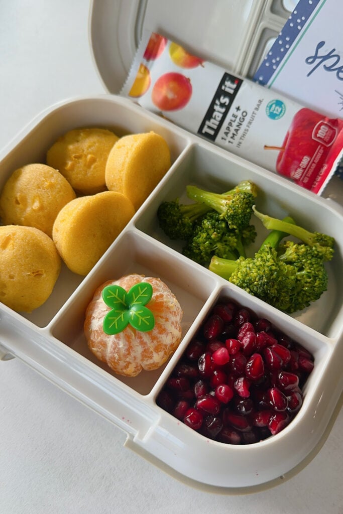 Corn muffins served with broccoli, mandarin, pomegranate seeds, and a that's it bar.