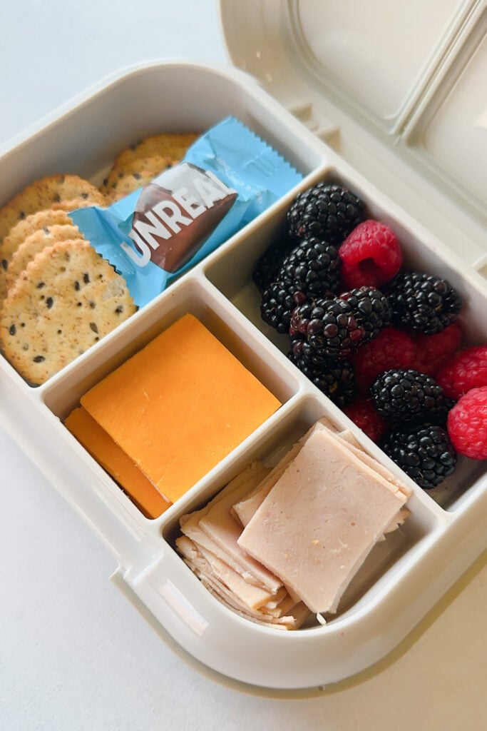 Crackers served with slice cheese, sliced turkey, blackberries, raspberries, and a mini chocolate bar.