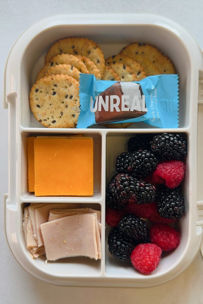 Crackers served with slice cheese, sliced turkey, blackberries, raspberries, and a mini chocolate bar.