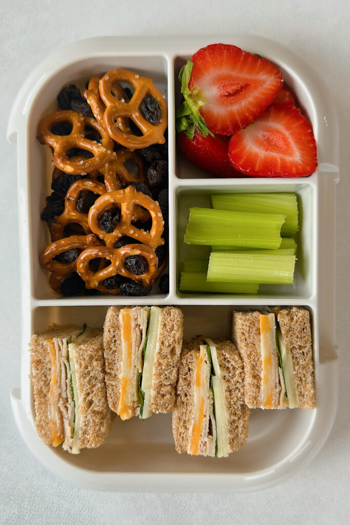 Mini turkey and cheese sandwiches served with pretzels, raisins, celery, and strawberries.