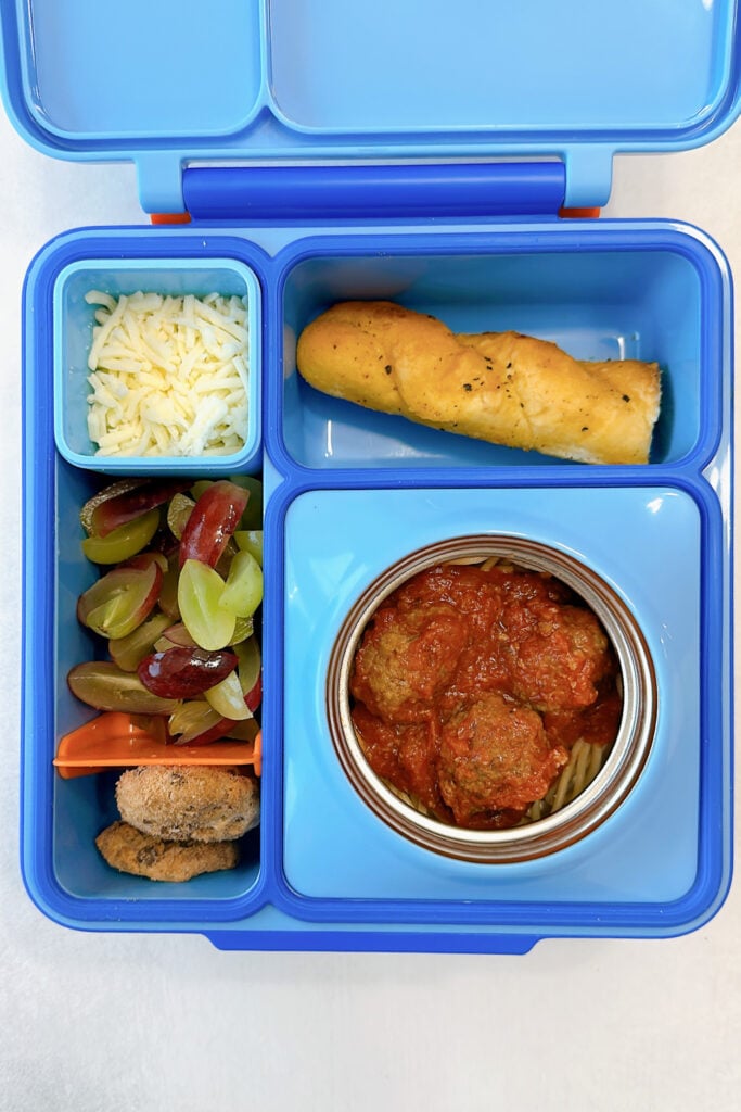 Spaghetti and meatballs served with a breadsticks, mozzarella cheese, grapes, and cookies.