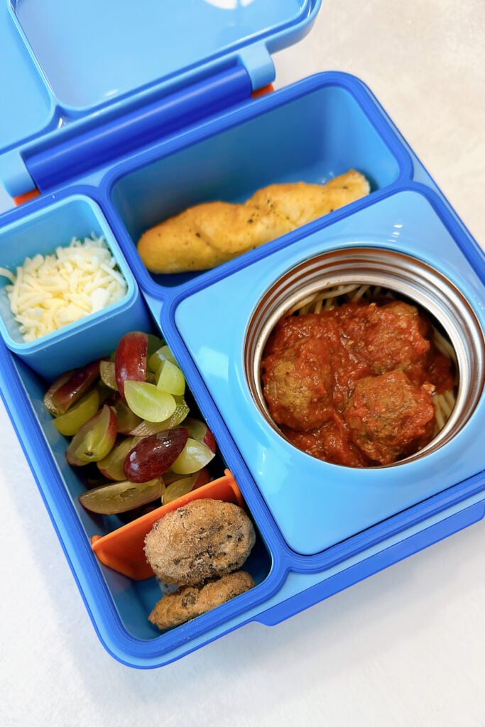 Spaghetti and meatballs served with a breadsticks, mozzarella cheese, grapes, and cookies.