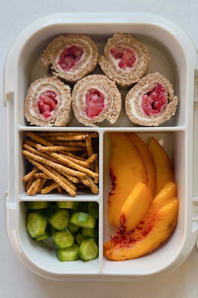 Strawberry and cream cheese rollups served with pretzels, cucumbers, and peaches.