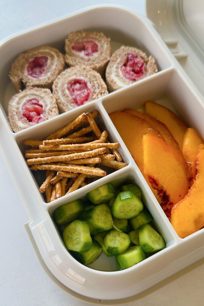 Strawberry and cream cheese rollups served with pretzels, cucumbers, and peaches.