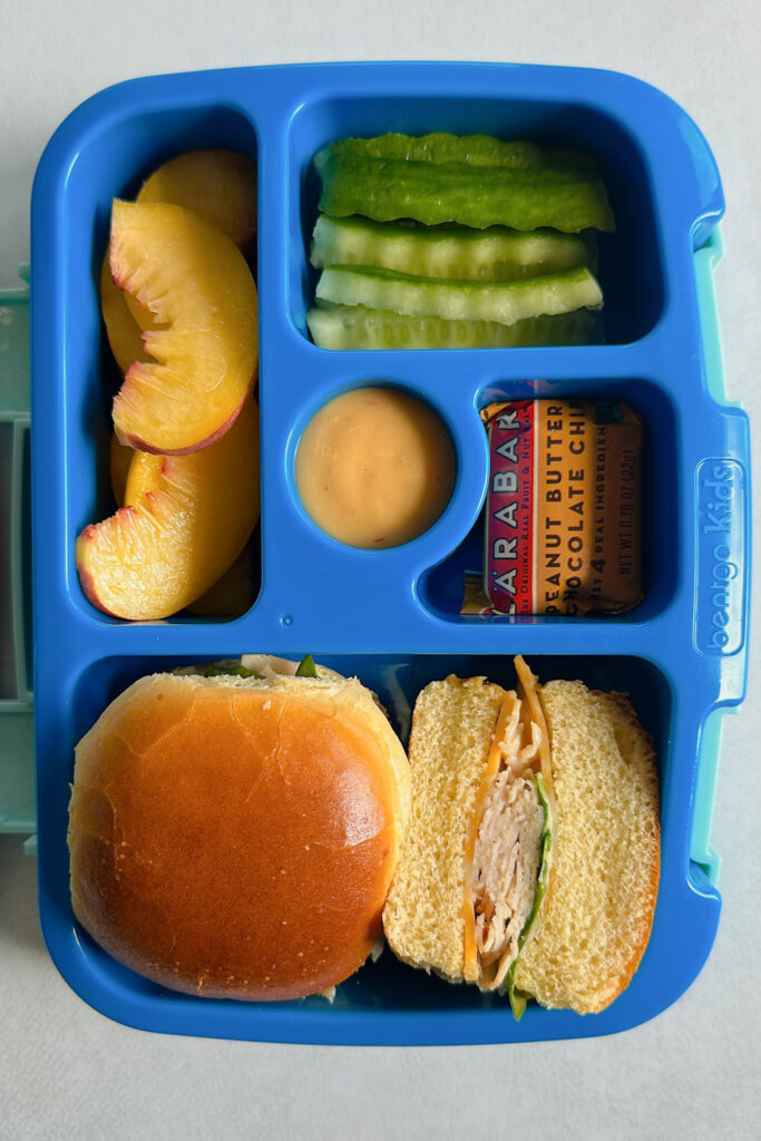 Turkey and cheese sliders served with sliced peaches, cucumbers, honey mustard, and a larabar.