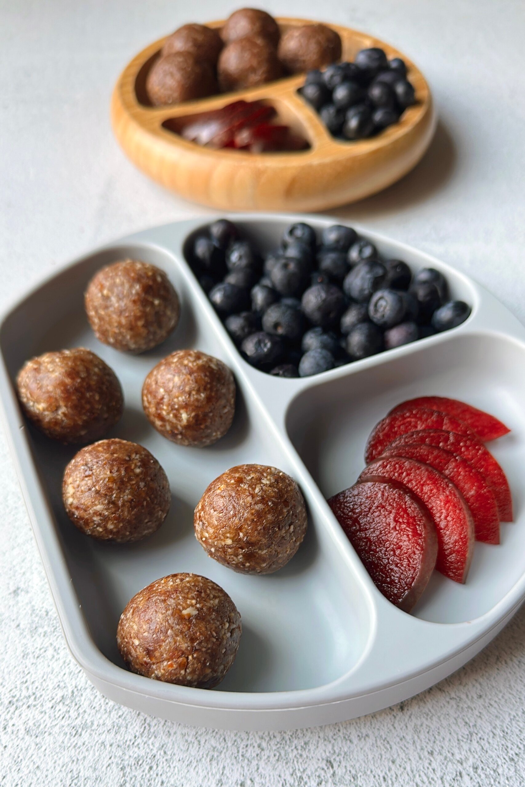 Date bites served with plums and blueberries.