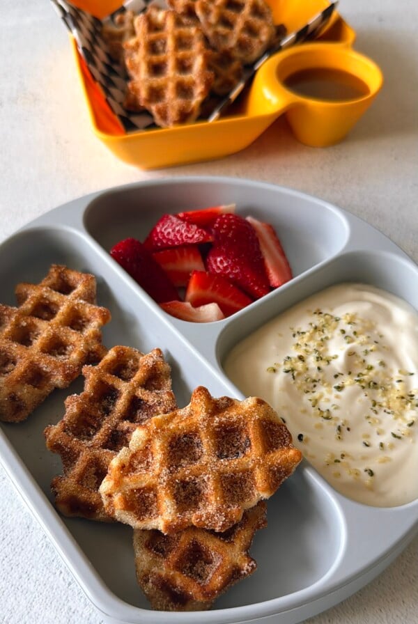 Banana waffle bites served with strawberries, yogurt, and a sauce for dipping.