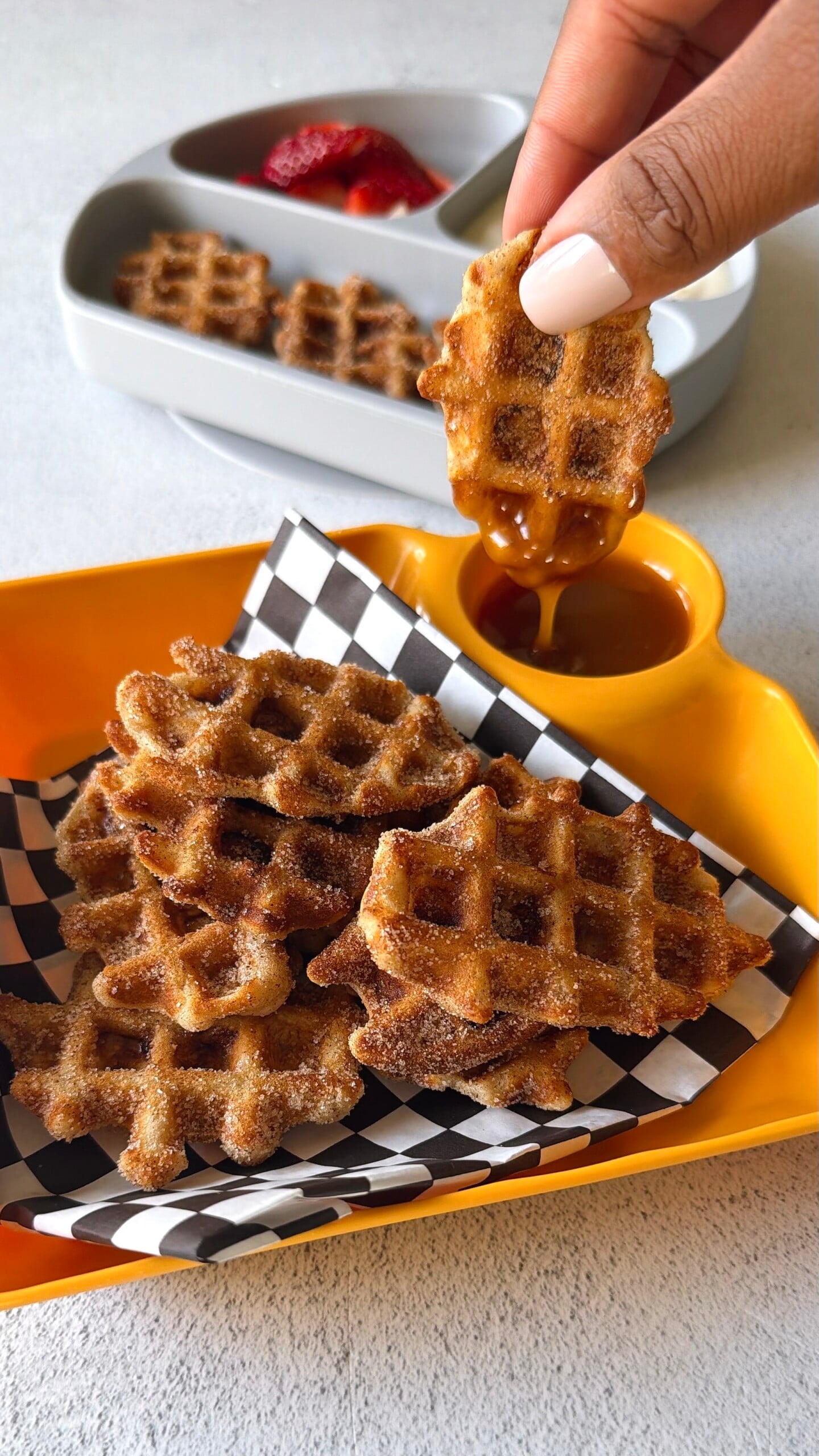 Banana waffle bites served with strawberries, yogurt, and a sauce for dipping.