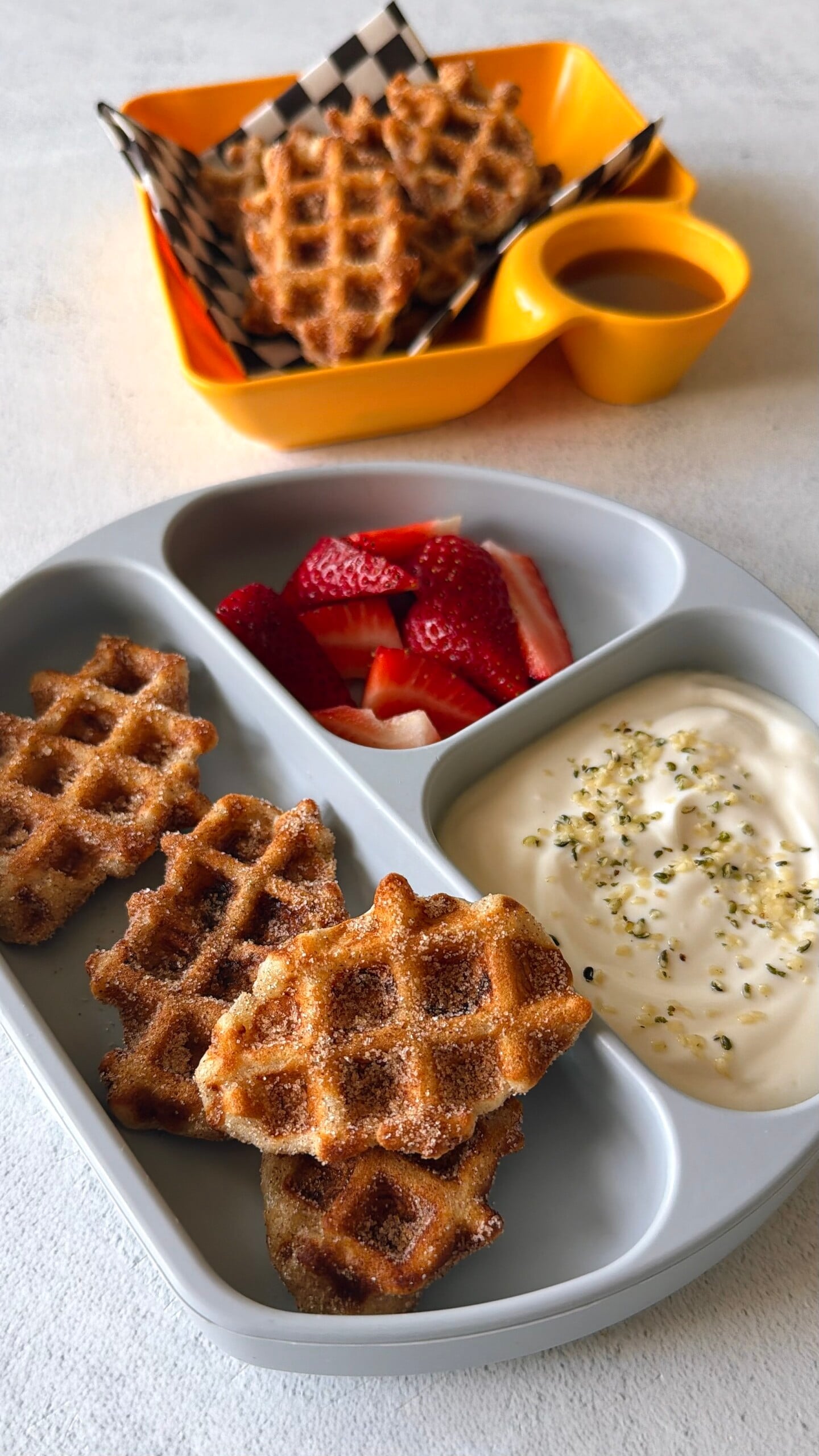 Banana waffle bites served with strawberries, yogurt, and a sauce for dipping.