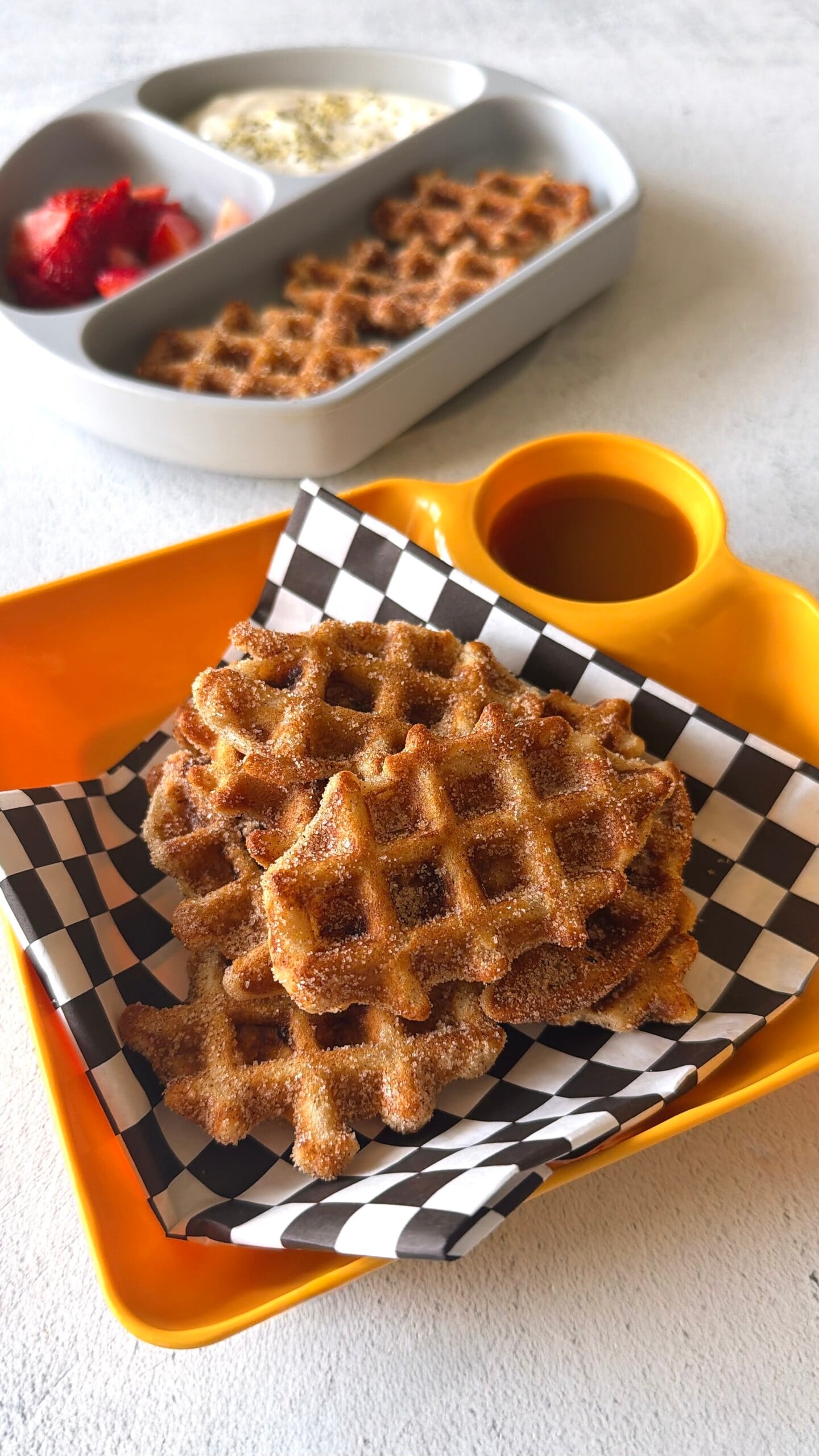 Banana waffle bites served with strawberries, yogurt, and a sauce for dipping.